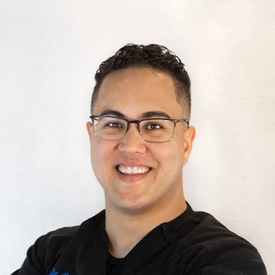 Chiropractor Eric Rivera Smiling In Front Of Grey Background